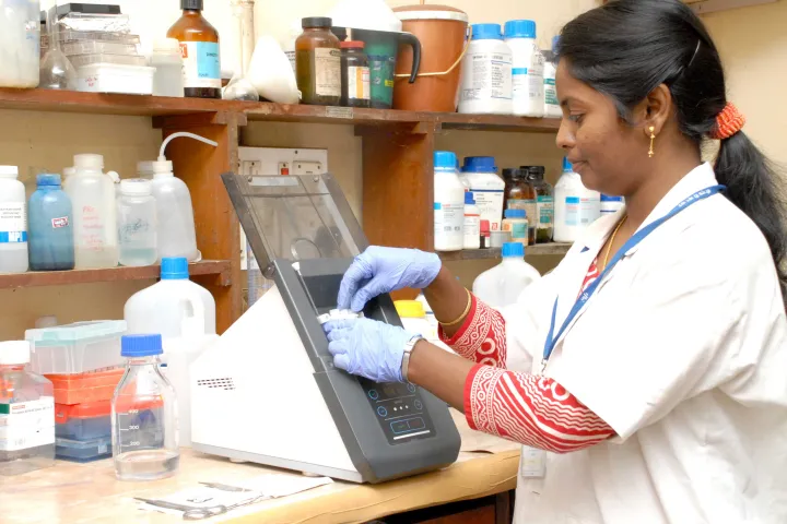 Research scholar in a lab coat and gloves operating an analytical instrument in a laboratory